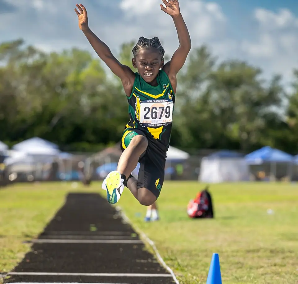 Long jumper with both arms raised in mid-air over the runway