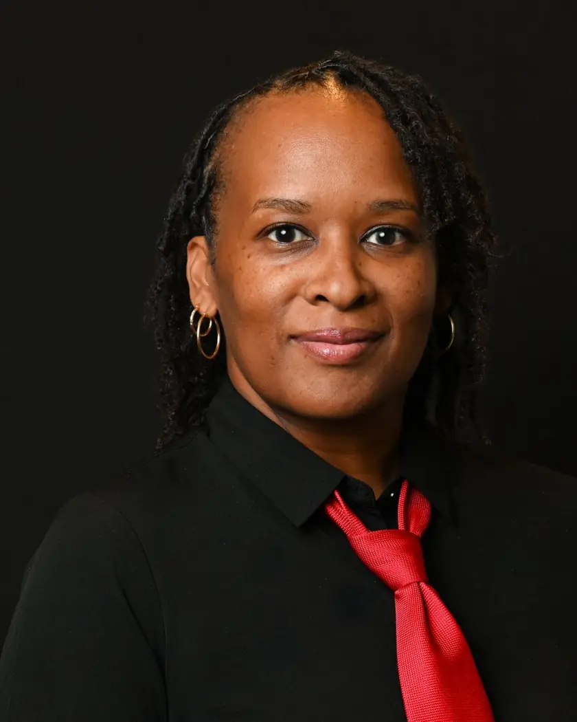 Tisha, founder of TD Sports Media, smiling in a black shirt and red tie